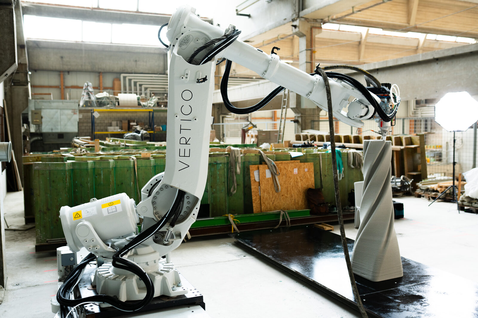 Sechsachsiger Roboter in der Halle, daneben eine gedruckte, in sich gedrehte Säule auf dem Druckbett